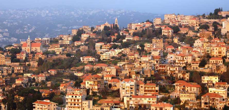 Panoramic view of Beit Chabab, Lebanon showing traditional Lebanese stone houses with red tile roofs cascading down the mountainside in golden hour lighting